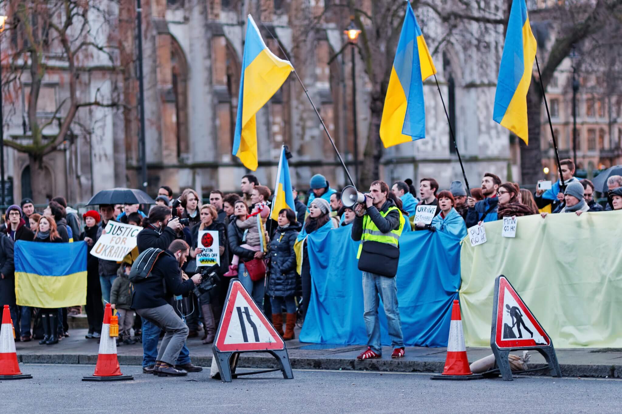 A group of protesters on a street wave Ukrainian flags and signs calling for justice for Ukraine.