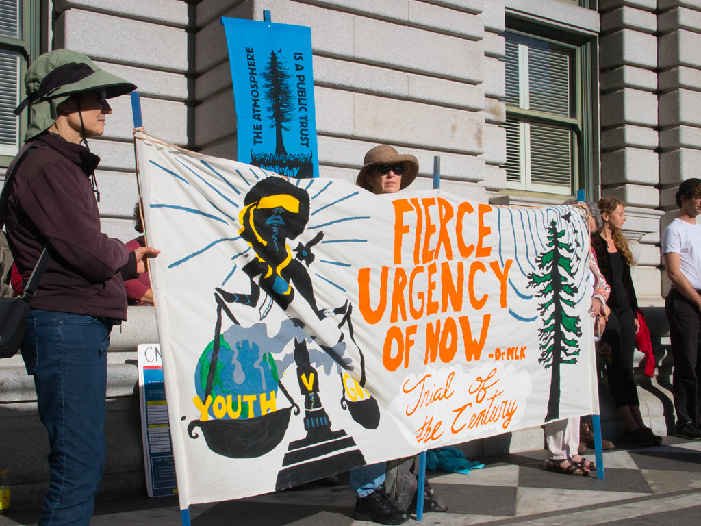 Protestors holding a sign depicting scales of justice and the Earth outside a courthouse.